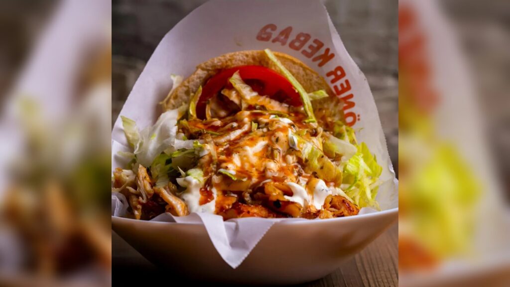 Nahaufnahme eines in Papier eingewickelten Hähnchen-Döner-Kebabs mit Salat, Tomaten und Saucen.