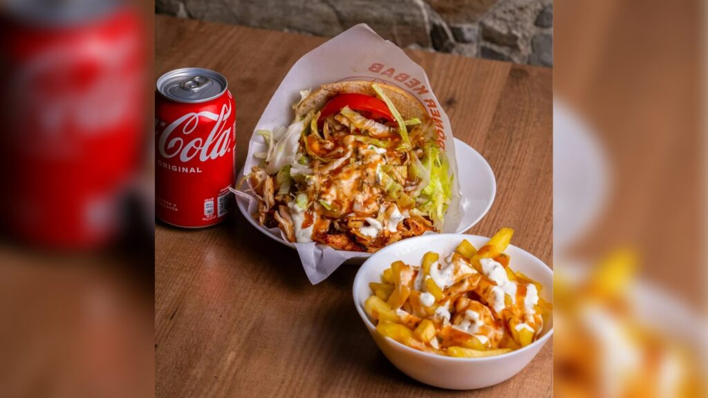 Ein verlockender Döner mit Pommes und einer erfrischenden Cola auf einem Holztisch.